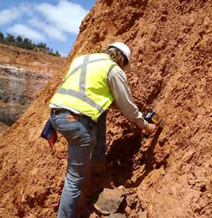 A field geochemist in a hi-vis vest using a portable XRF analyser against an exposed laterite face in an exploration trench