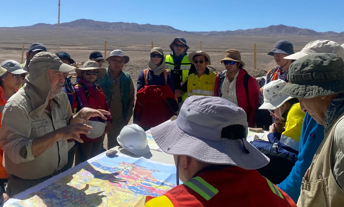 A field trip leader explaining regional geology from a map to AAG members gathered around him in the desert