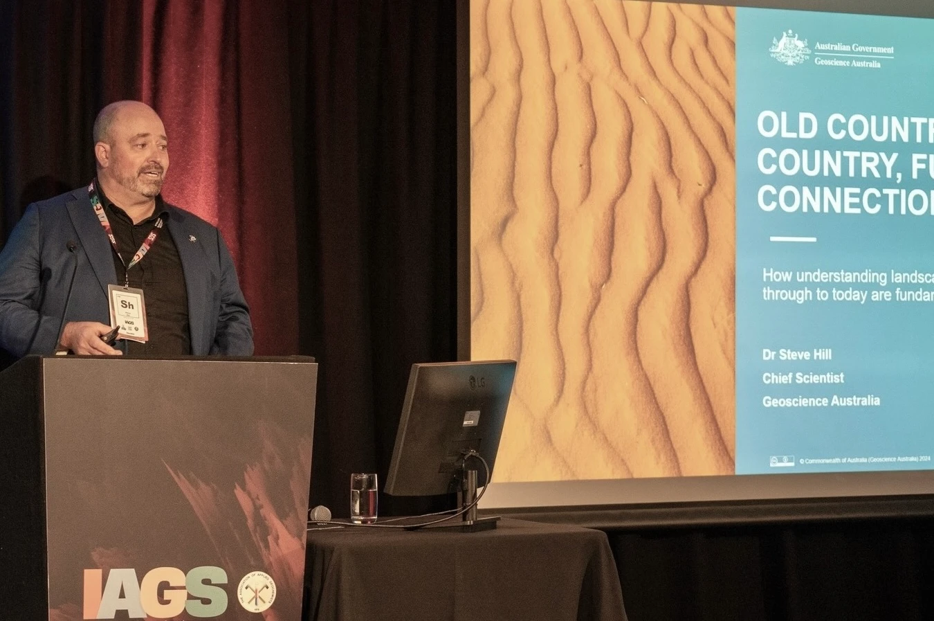A speaker delivering a keynote address from the podium at an International Applied Geochemistry Symposium
