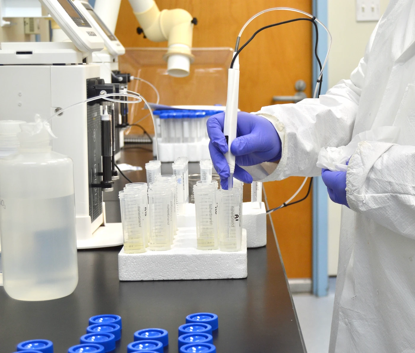 A technician in a clean suit pipetting prepared geochemical samples into tubes in an analytical laboratory